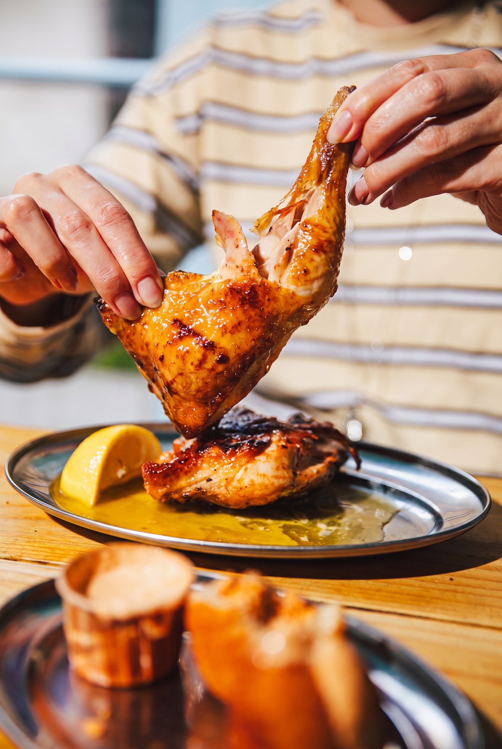 Handen scheuren een halve kip van de grill boven een bord met citroen en piri-piri-saus