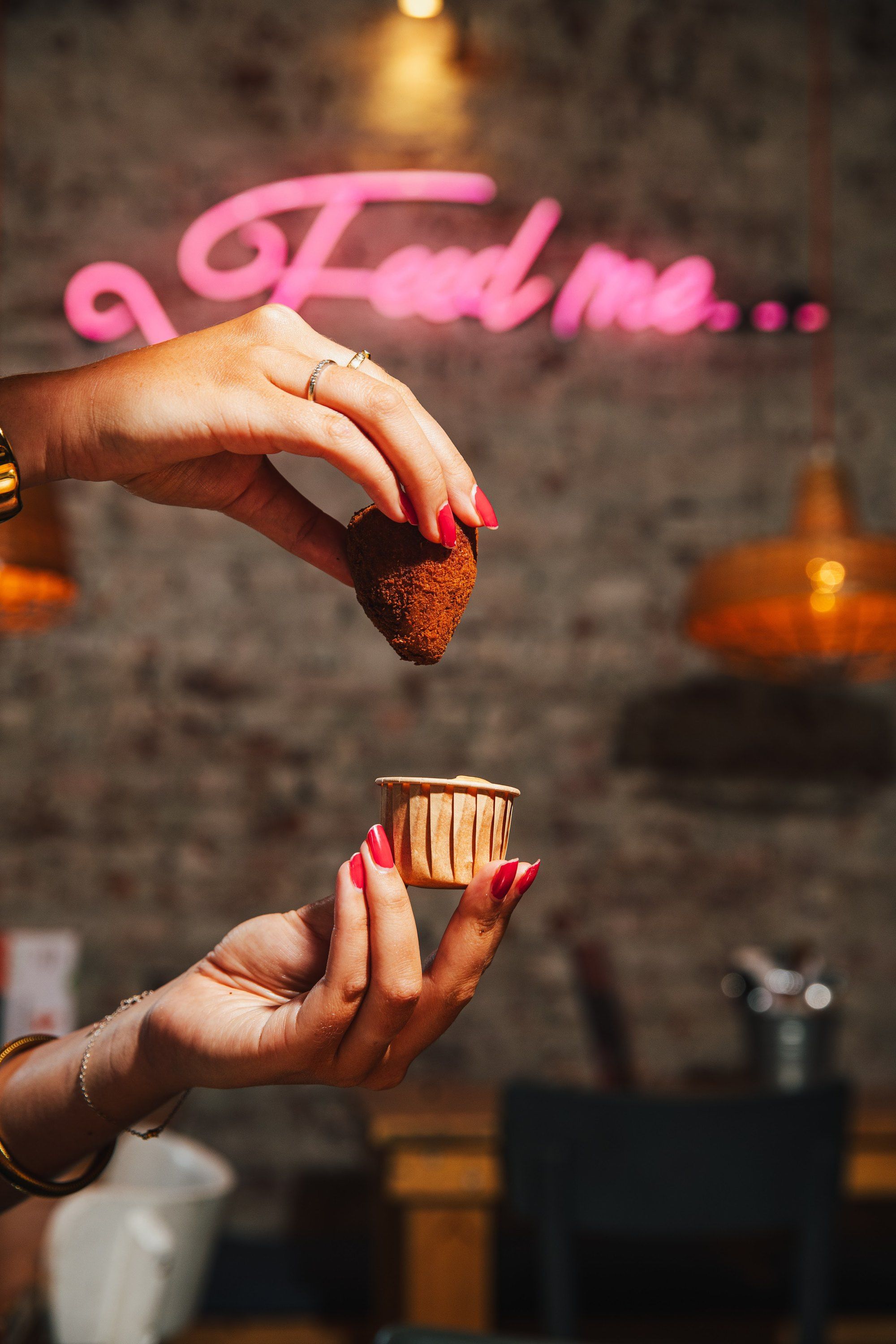 Een coxinha met dip onder de neon “Feed me” bij Franggo West